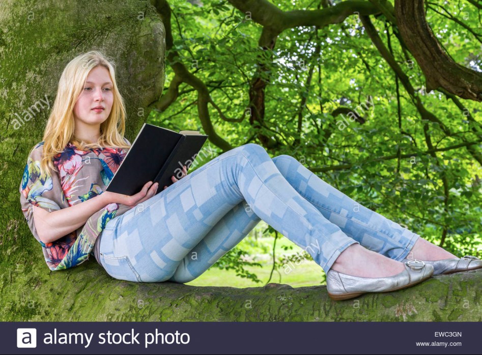blonde-caucasian-teenage-girl-lying-on-green-tree-reading-book-EWC3GN.jpg